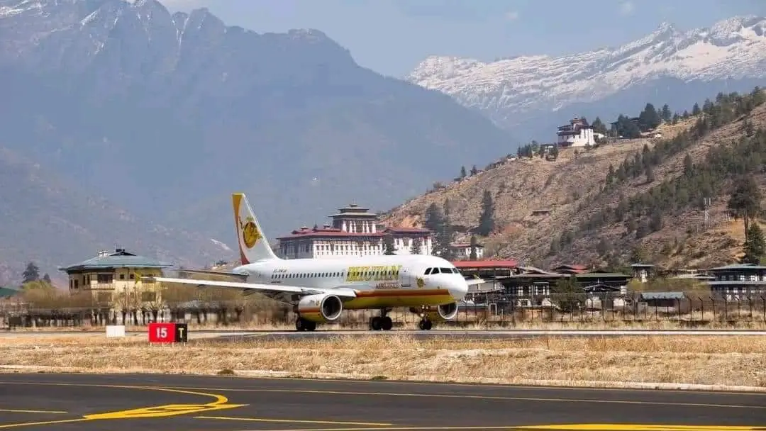 Druk Air airplane taxiing on the runway at Paro International Airport in Bhutan, surrounded by traditional Bhutanese architecture and Himalayan mountains