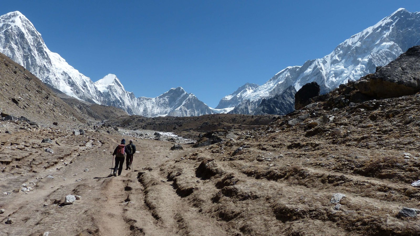 Trekkers walking through a scenic mountain valley surrounded by high peaks and alpine landscapes.