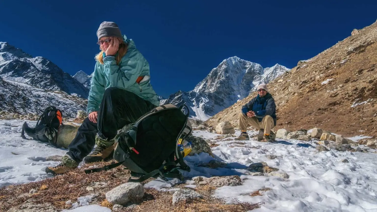 Adventure travel bloggers and explorers resting on a snowy Himalayan trail during a trek in Nepal, inspired by ThePlanetD founders Deb Corbeil