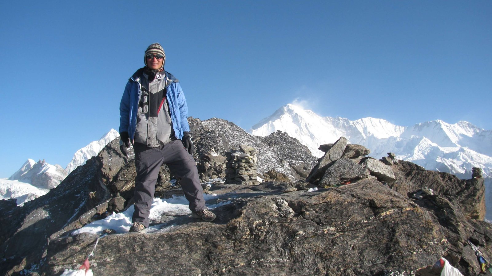 A trekking guide standing at the top of Gokyo Ri with panoramic views of snow-covered Himalayan peaks under a clear blue sky
