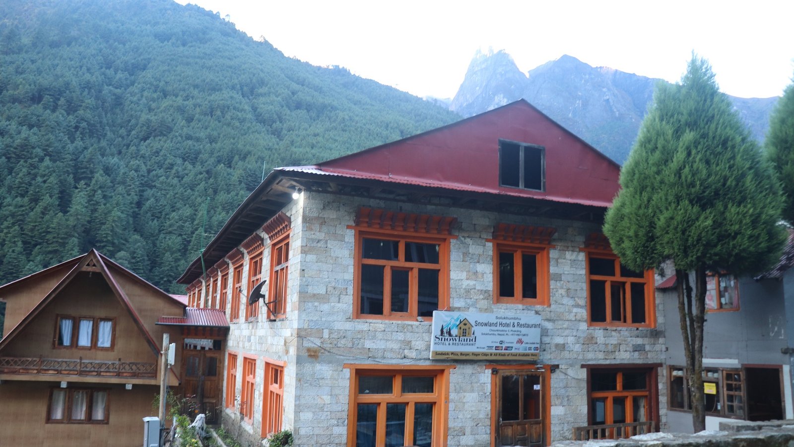 Traditional stone lodge in the Everest region along the Jiri to Everest Base Camp trekking route, surrounded by pine forests and Himalayan mountains.