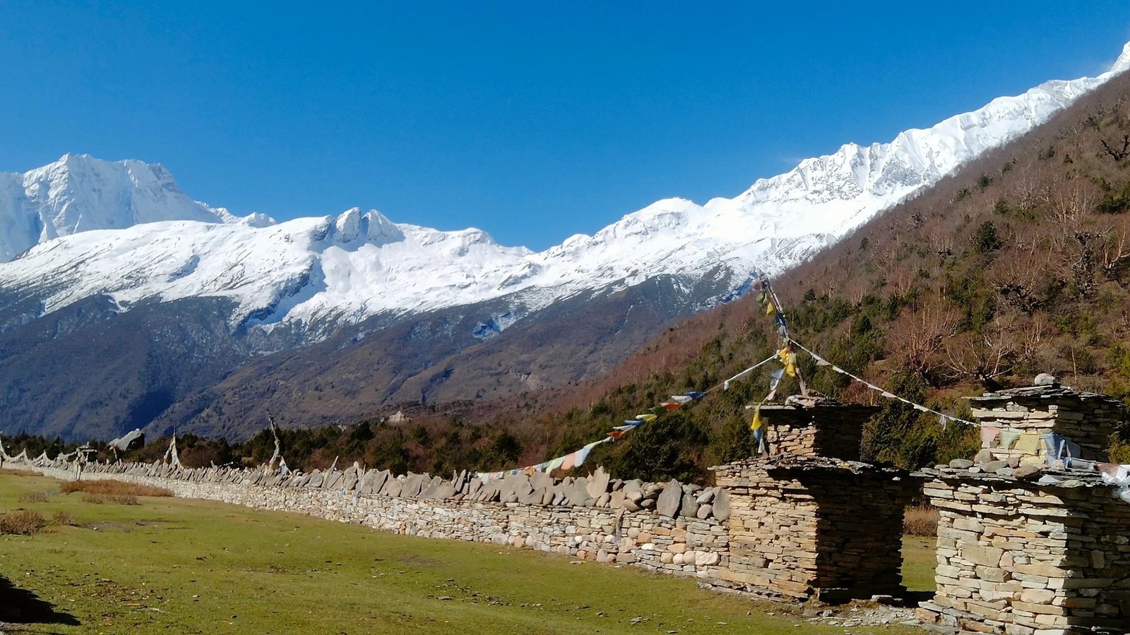 Long Mani wall on the Manaslu Circuit Trek route from Samagaon to Samdo, featuring Tibetan Buddhist stone carvings, prayer flags, and a dramatic Himalayan mountain landscape in Nepal.