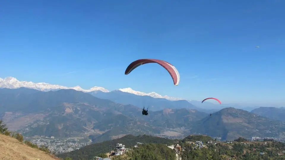 Paragliding in Nepal over scenic Himalayan landscapes with panoramic mountain views, green hills, and clear blue sky