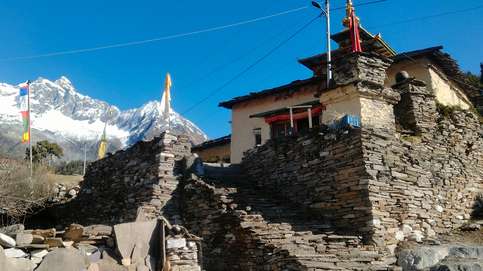 Samagaon monastery in Manaslu region with ancient stone structure, prayer wheels, and panoramic mountain views in Nepal.