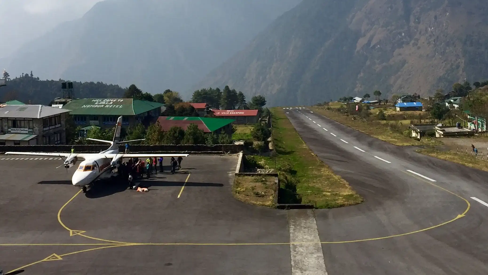 Tenzing-Hillary Airport in Lukla with a small aircraft on the runway, surrounded by Himalayan mountains under a clear blue sky
