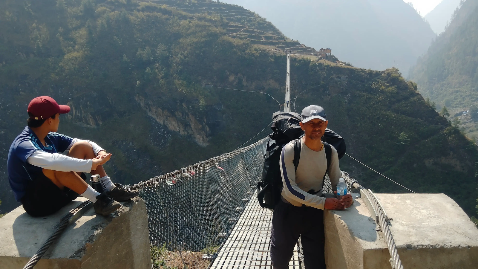 Trekkers crossing a suspension bridge at Bihi Village on the Manaslu Circuit Trek, surrounded by a river gorge and Himalayan mountain scenery in Nepal.