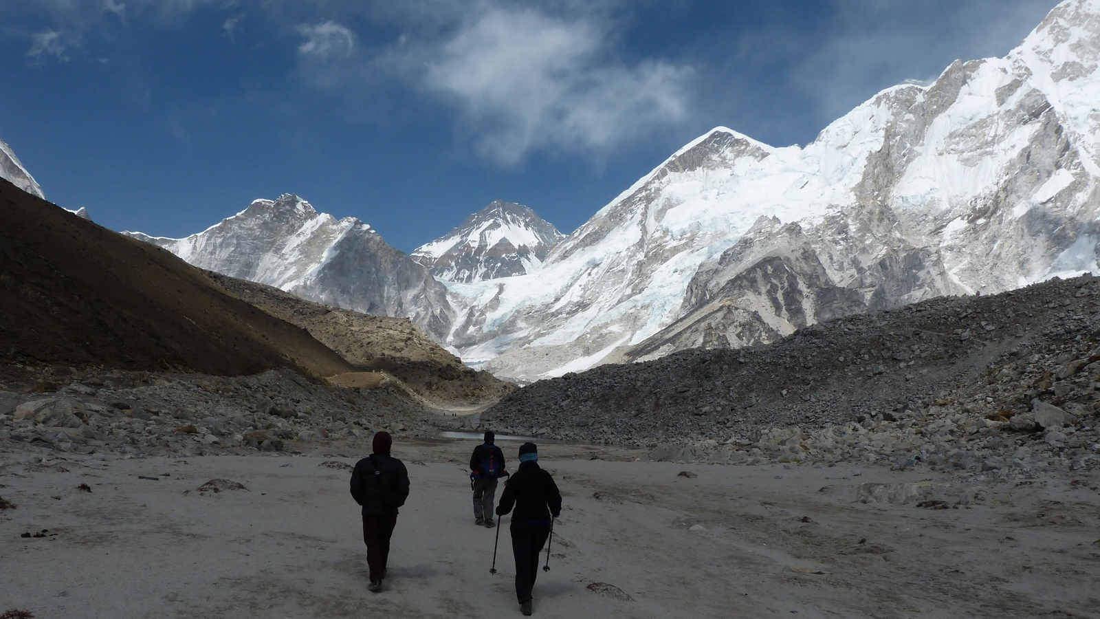 Trekkers walking towards Everest Base Camp with a clear view of Mount Everest and surrounding snow-covered Himalayan peaks under a bright blue sky.