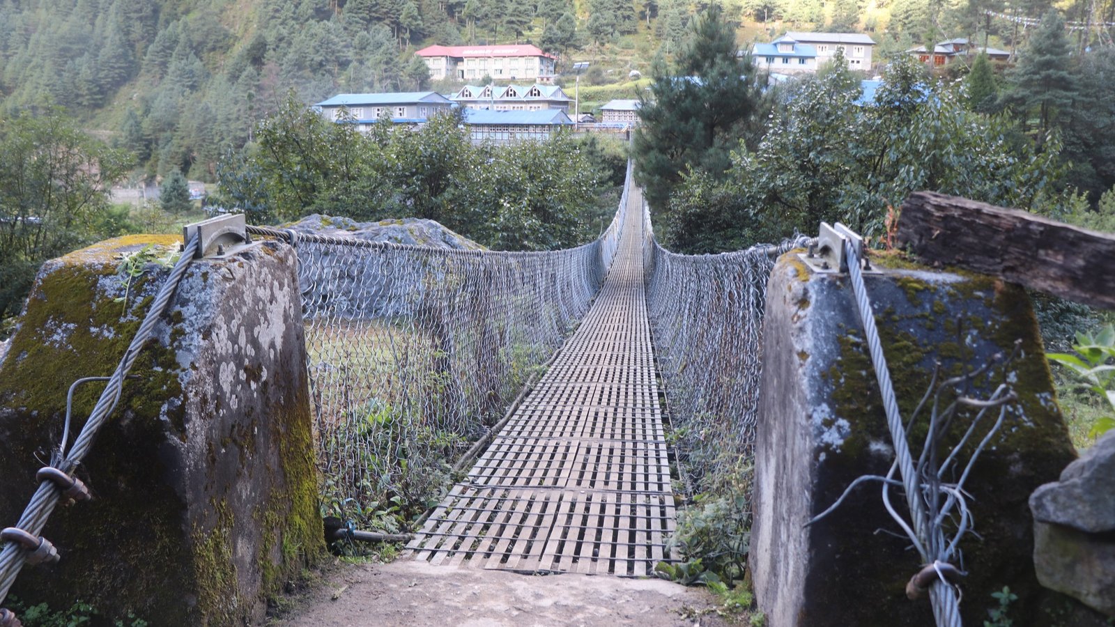 Suspension bridge on the Jiri to Everest Base Camp trekking trail, surrounded by lush green hills and traditional villages in the Solu region of Nepal.